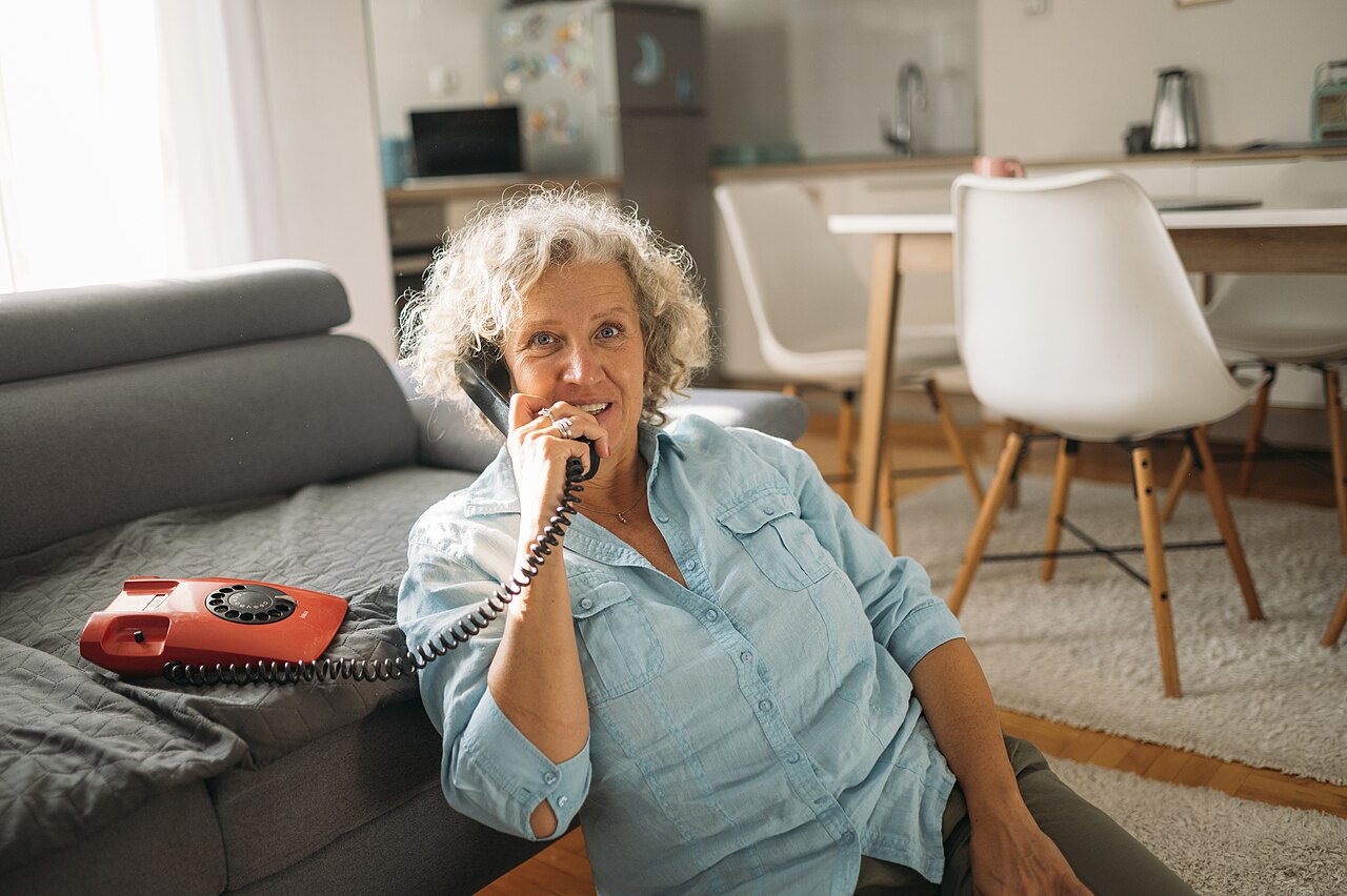 An older woman talks on a telephone at home